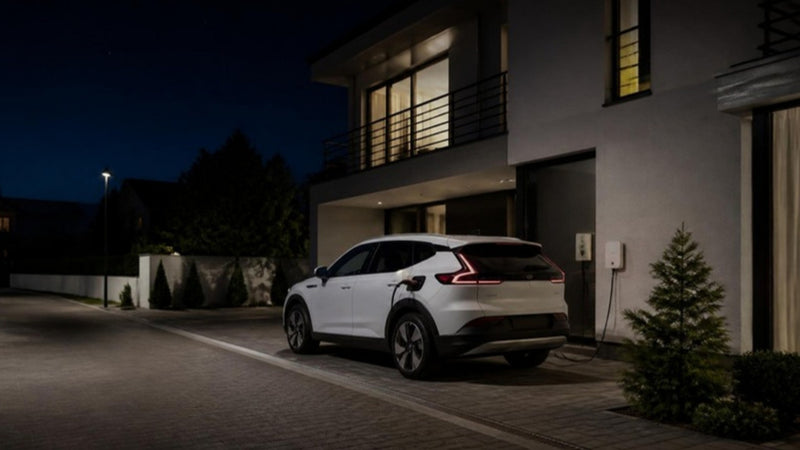 Gece saatlerinde evin önünde duvar tipi şarj cihazına bağlı, şarj olan beyaz elektrikli SUV